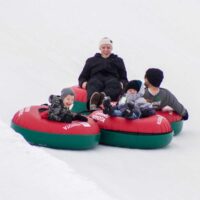 A joyful family of four sliding down a snowy slope on connected red and green snow tubes capturing the thrill of winter fun The smiling parents and excited children embody the spirit of family bonding in a pristine snowy landscape My local utah