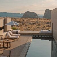 A tranquil desert poolside scene featuring modern lounge chairs a wooden table and a sleek infinity pool reflecting the arid landscape and distant rock formations The minimalist design and natural surroundings offer a peaceful retreat ideal for a luxurious day of relaxation in the desert My local utah