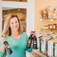 Eat Local Mountain Town Olive Oil Park City Utah | My Local Utah Local utah business owner holding a selection of premium olive oils including flavored varieties like garlic and rosemary at mountain town olive oil My local utah
