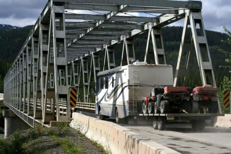 image of a couple of ATVs strapped down to a trailer- being hauled by a RV going through a bridge across the canyon