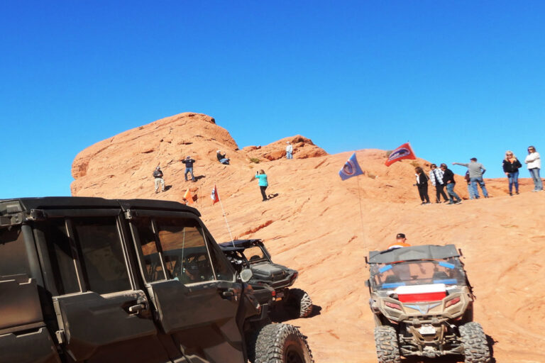 Group of people and their ATVS on top of the peak of the red rock, posing for a picture.
