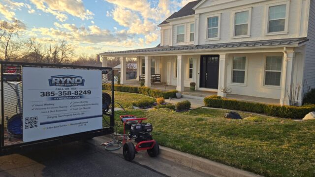 Two-story white house with a front porch, visible service sign in the driveway reading Ryno Wash Services and a few cleaning tools nearby (late afternoon light).