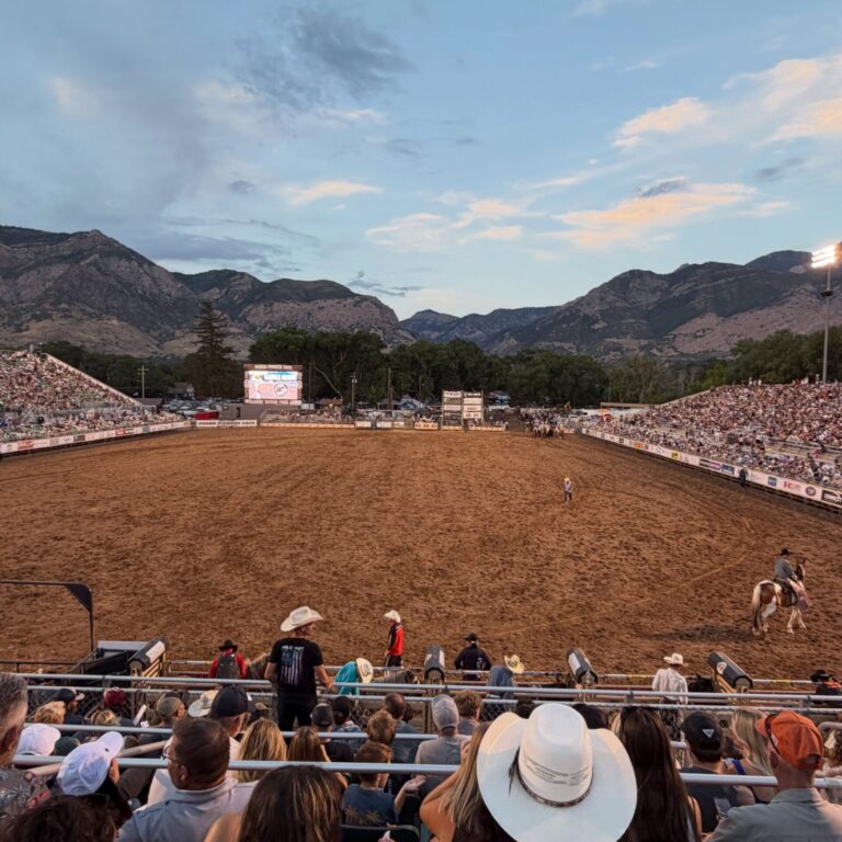 Ogden Pioneer Days Rodeo Outdoor rodeo arena plein with dirt track, grandstands full of spectators, and mountain range in the background at dusk.